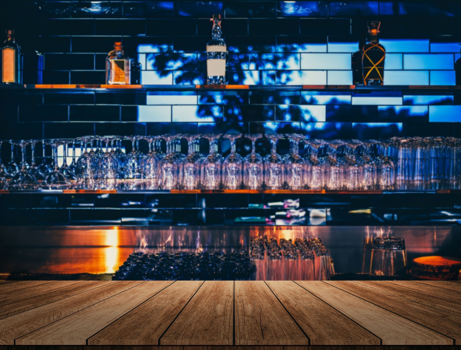 Bar avec des rangées de verres et un éclairage bleu-orange au-dessus d'un sol en bois.