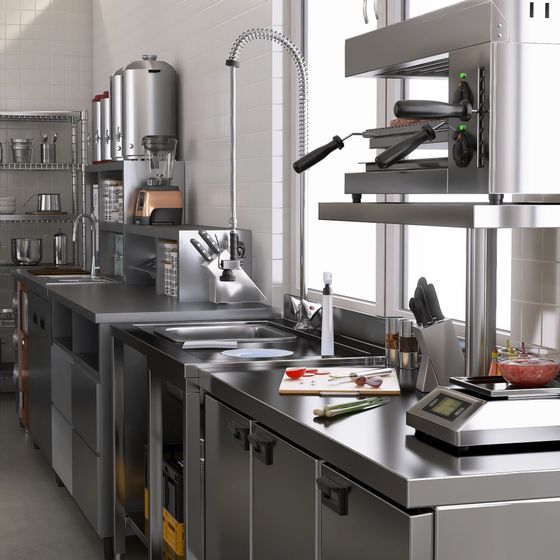 Cuisine professionnelle en acier inoxydable avec comptoirs, machine à expresso, ustensiles et batterie de cuisine sous un éclairage vif.