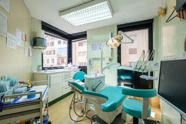 Una sala de exploración dental con un sillón color turquesa, instrumental dental, un armario blanco