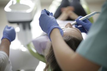 Un profesional dental, con guantes azules, realiza un procedimiento a un paciente que yace en un sillón dental.