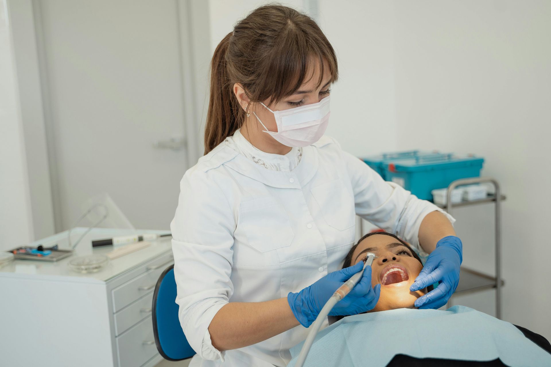 Un profesional sanitario, con mascarilla y guantes azules, realiza un procedimiento dental a un paciente en una clínica.