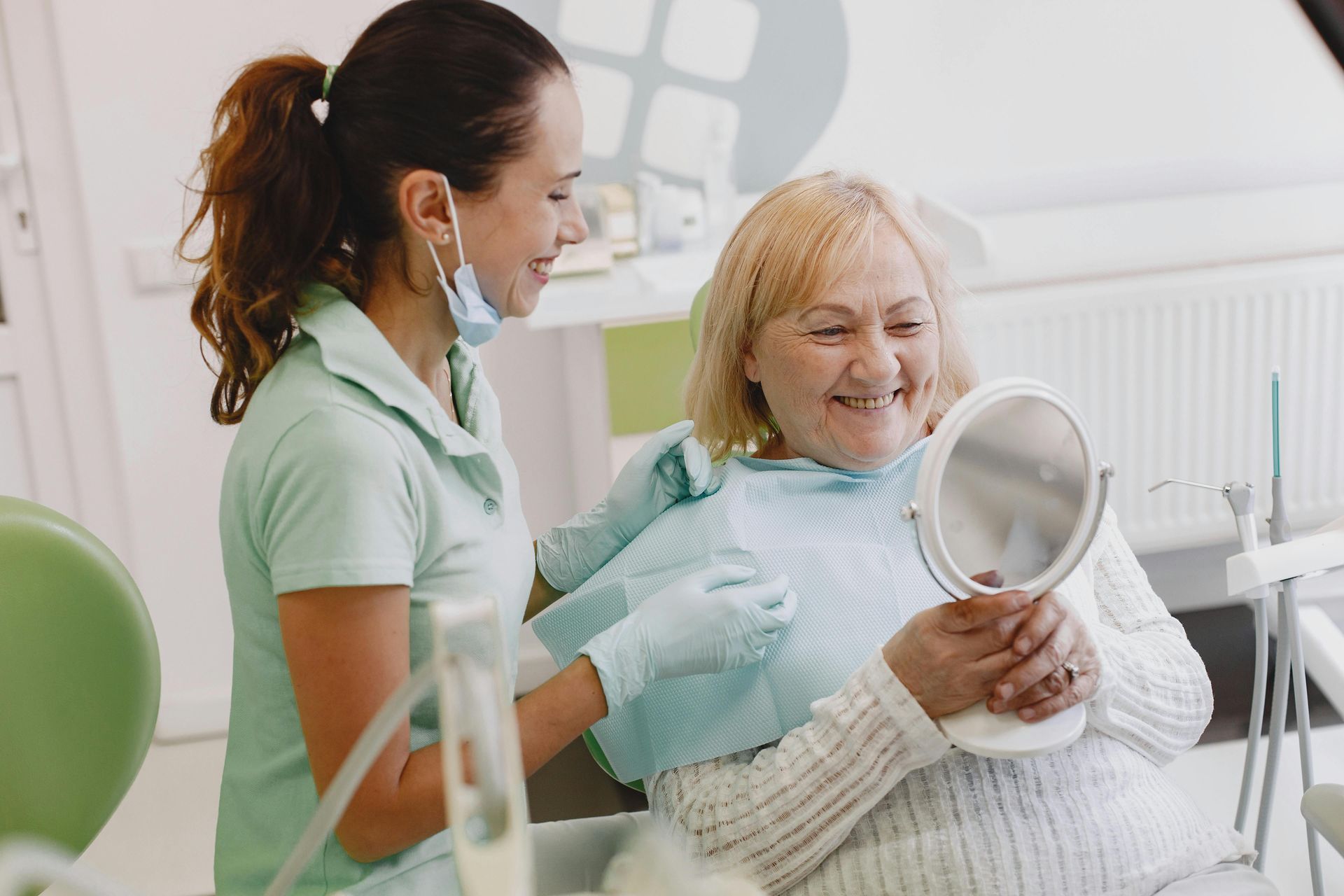 En una clínica dental, un profesional con uniforme verde le muestra a un paciente sonriente 