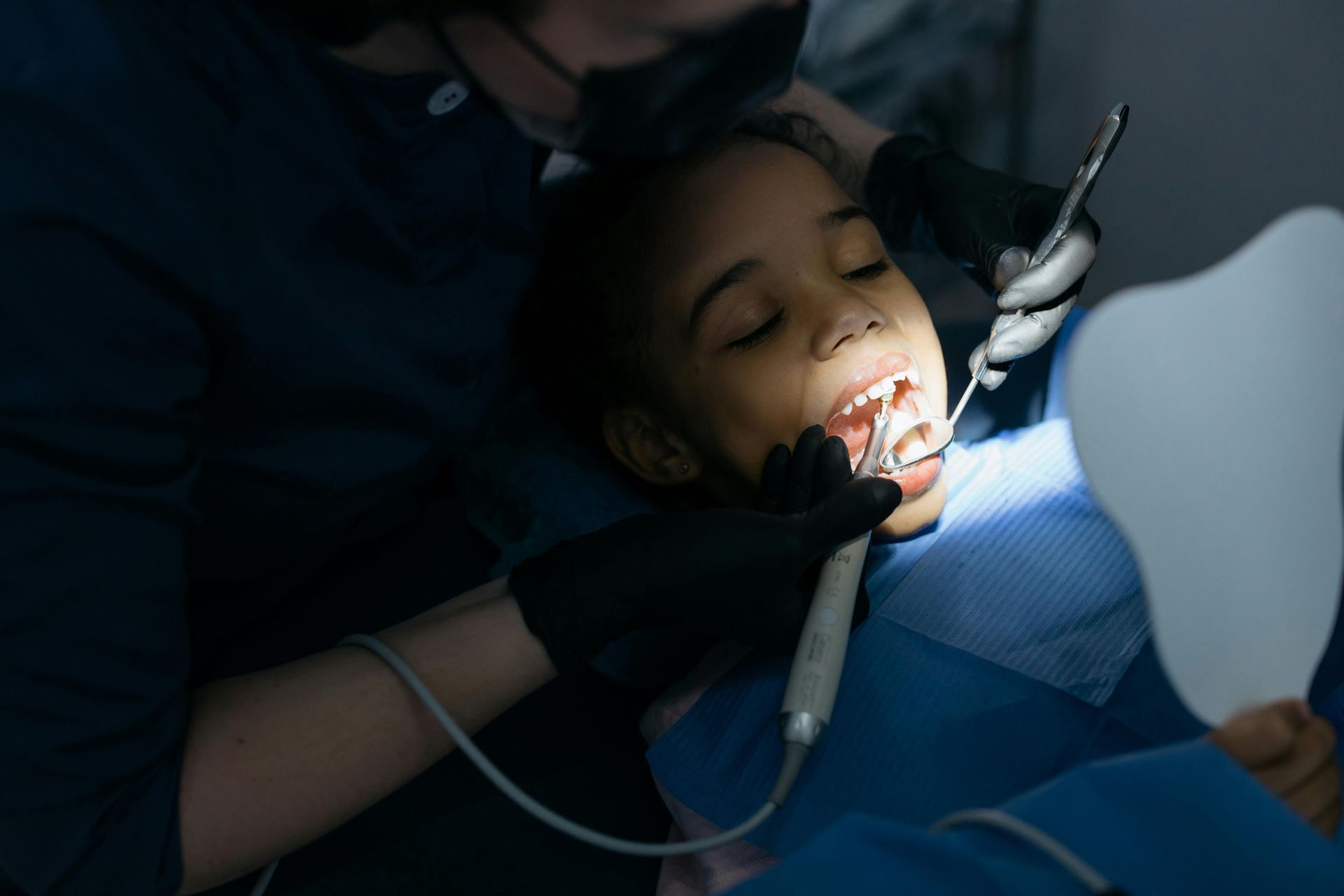 Un dentista con bata negra y guantes examina los dientes de un paciente con herramientas