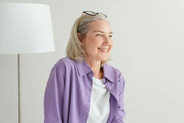 Una persona sonriente, vestida con una camisa morada y gafas en la cabeza