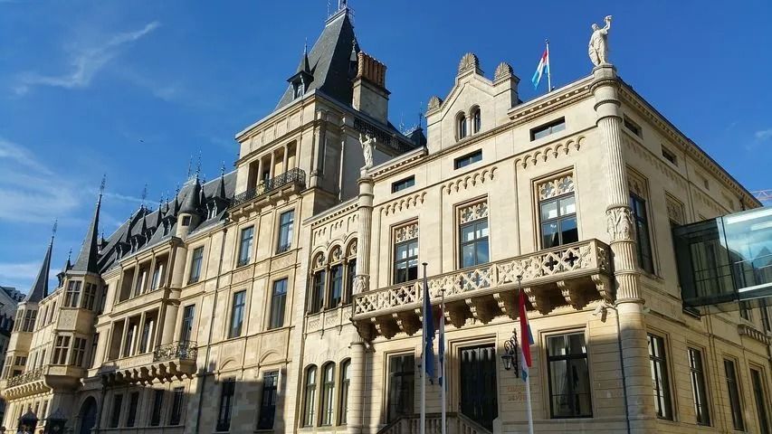 Vue extérieure de l'hôtel de ville de Luxembourg, un bâtiment orné de couleurs claires, avec des drapeaux.
