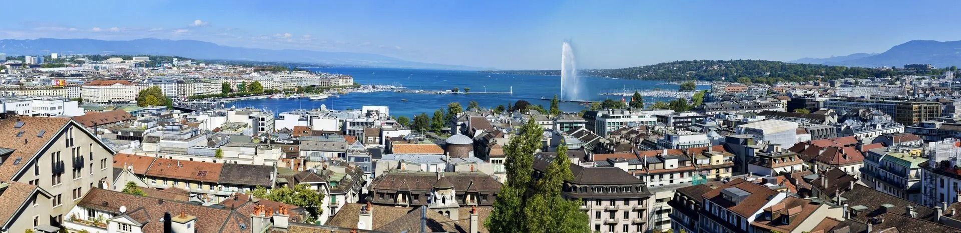 Vue panoramique de Genève, en Suisse, avec ses bâtiments, son lac et sa fontaine. Montagnes à l'horizon.