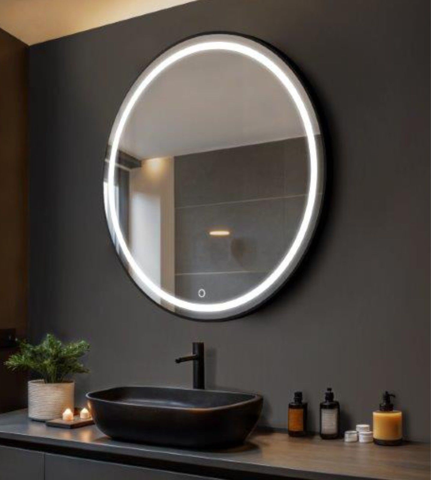 Tocador de baño moderno con espejo redondo retroiluminado, lavabo negro y velas en una pared oscura.