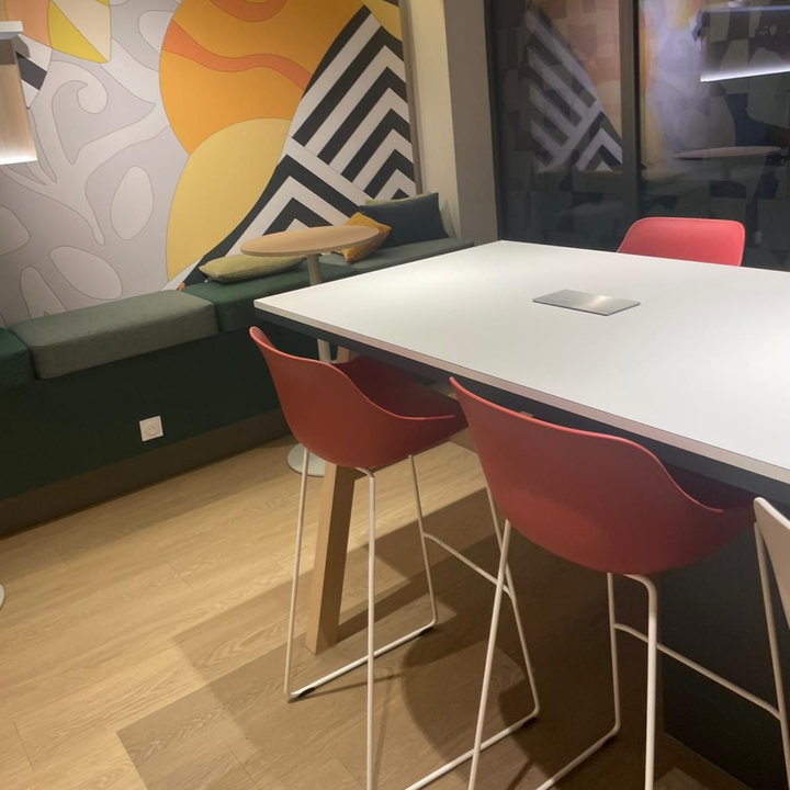Coin café moderne avec une table blanche, des chaises rouges, un banc vert et une fresque murale géométrique.