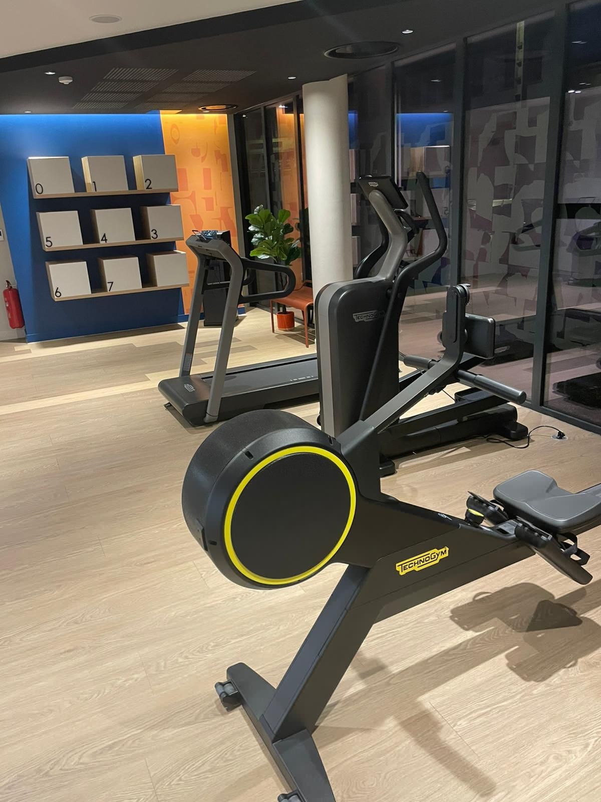 Intérieur d'une salle de sport moderne avec une rangée d'appareils de musculation et un rameur assis au premier plan.