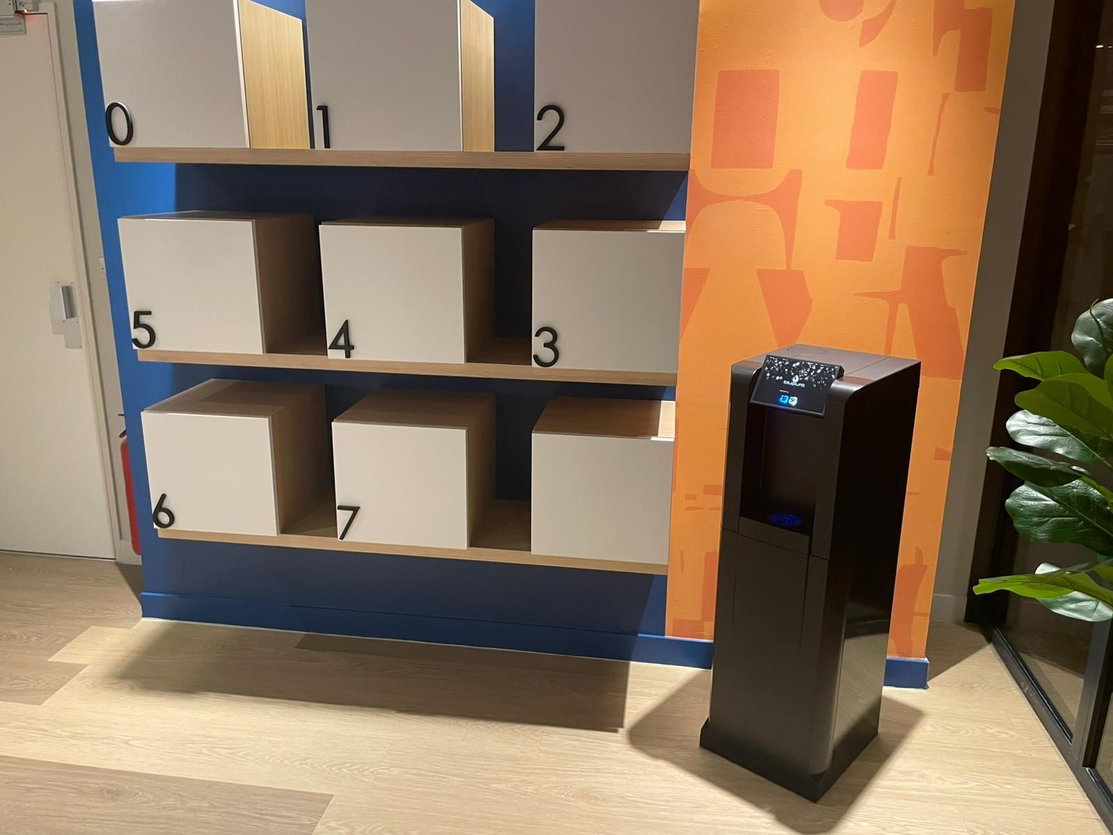 Des casiers numérotés de 1 à 6 sont disposés à côté d'une borne noire dans un hall.