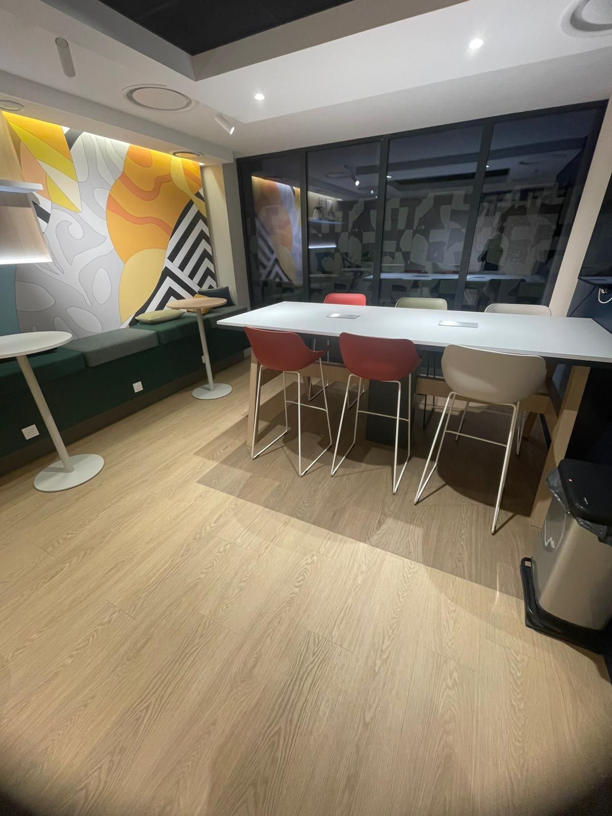 Salon de bureau moderne avec une longue table blanche, des chaises, des bancs et une œuvre d'art murale abstraite.