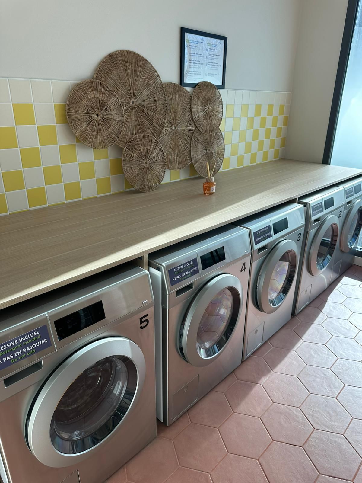 Buanderie avec lave-linge en inox sous un plan de travail et crédence en carrelage à damier jaune.