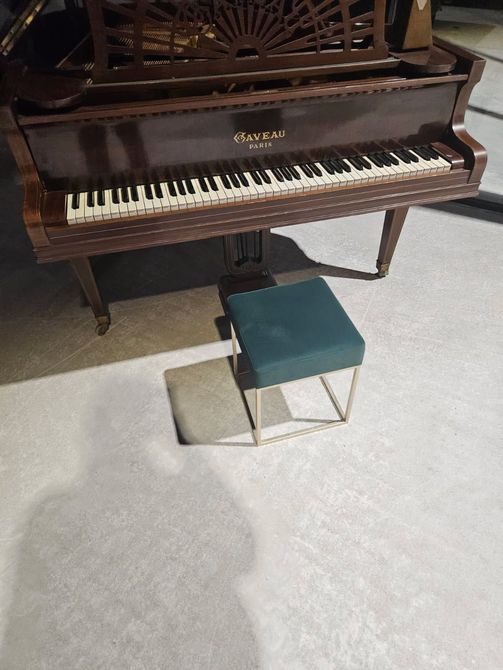 Piano en bois foncé avec banquette rembourrée turquoise sur un sol recouvert de moquette claire.