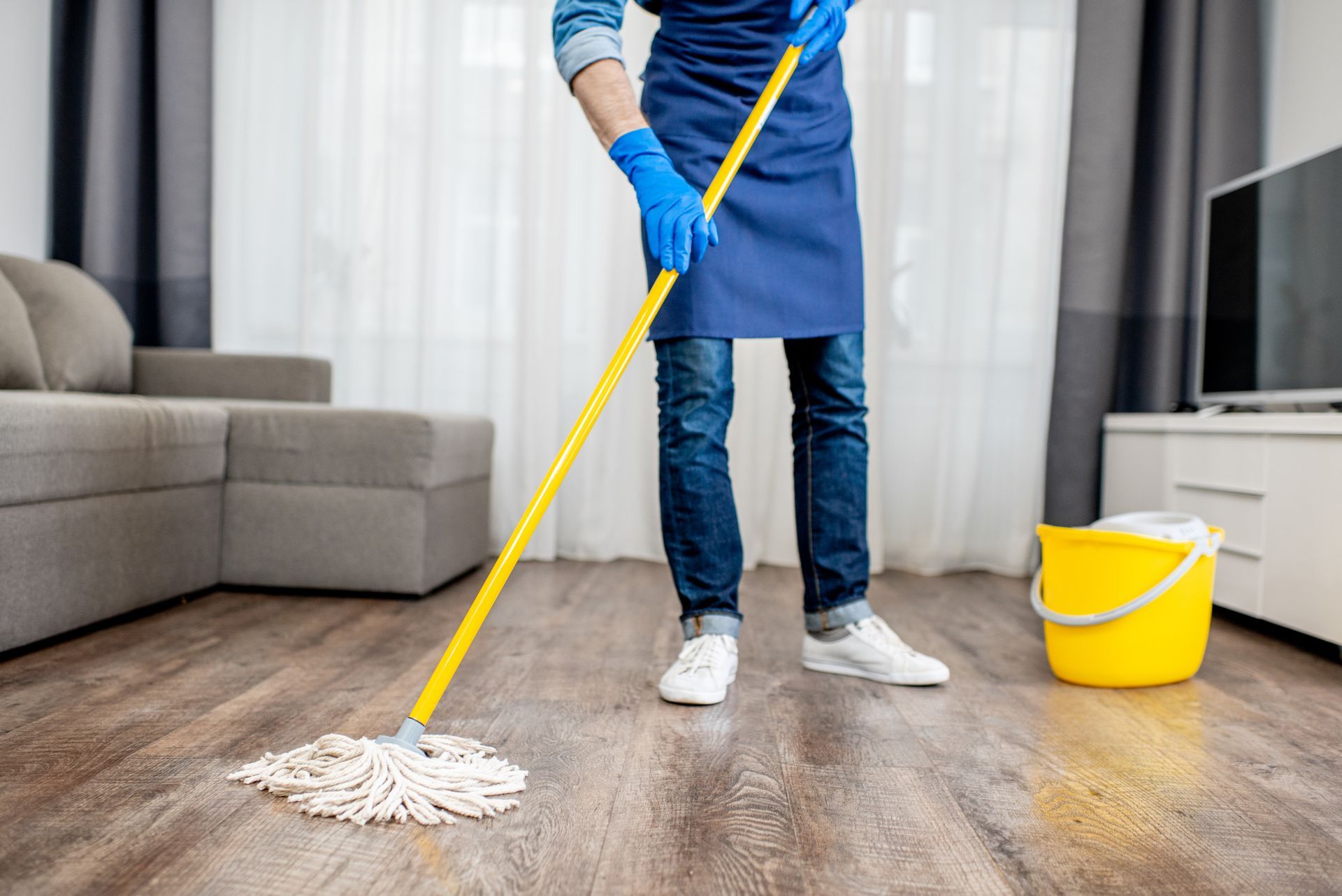 Une personne lave le parquet d'un salon à côté d'un seau jaune.