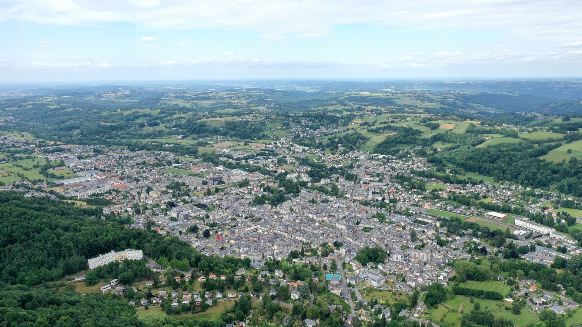 Vue aérienne d'une grande ville entourée de collines verdoyantes et de champs sous un ciel brumeux