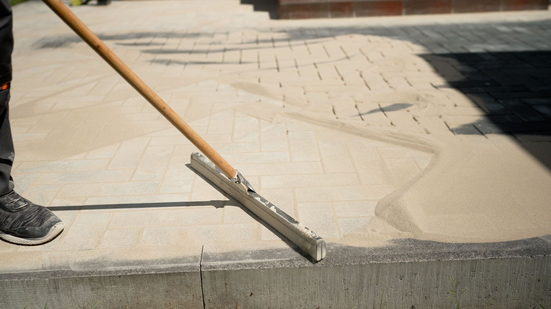 Un ouvrier lisse du béton frais avec un outil à long manche le long d'un trottoir.