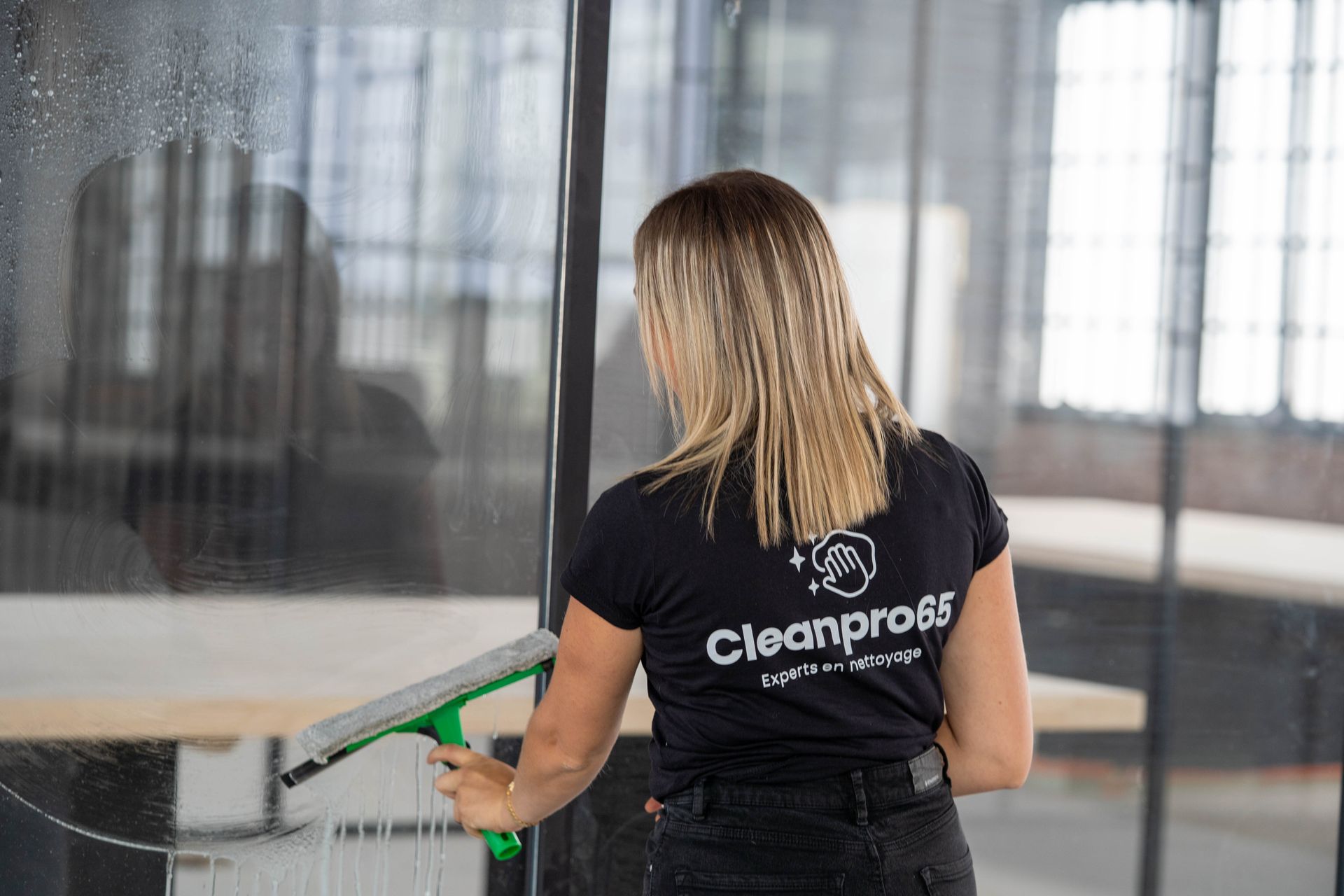 Un homme en uniforme de travail noir tient un chiffon de nettoyage jaune, se détachant sur un fond blanc.