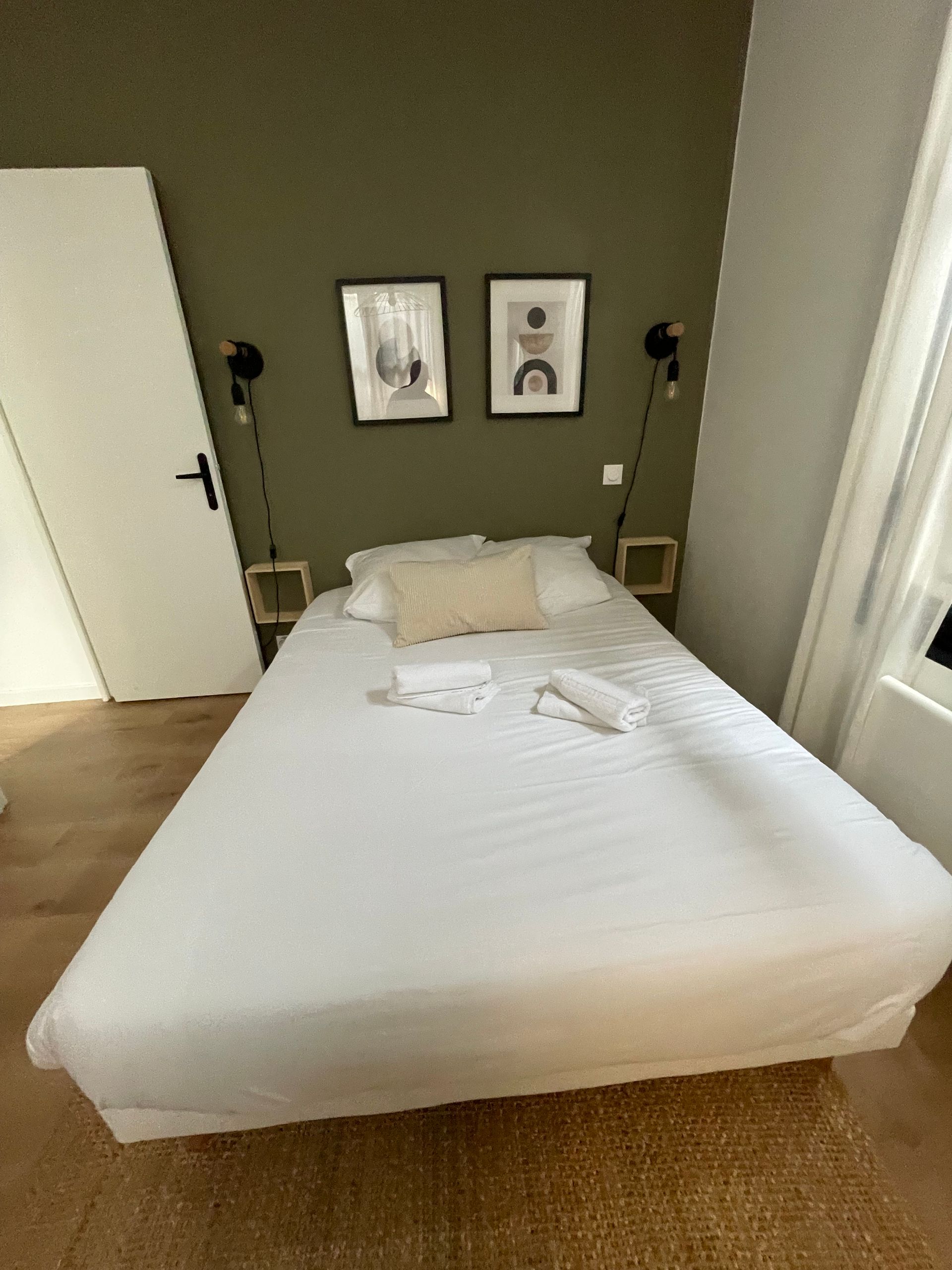 Pièce baignée de soleil avec des ombres rayées sur le parquet, des serviettes pliées à gauche et des voilages près de la fenêtre.
