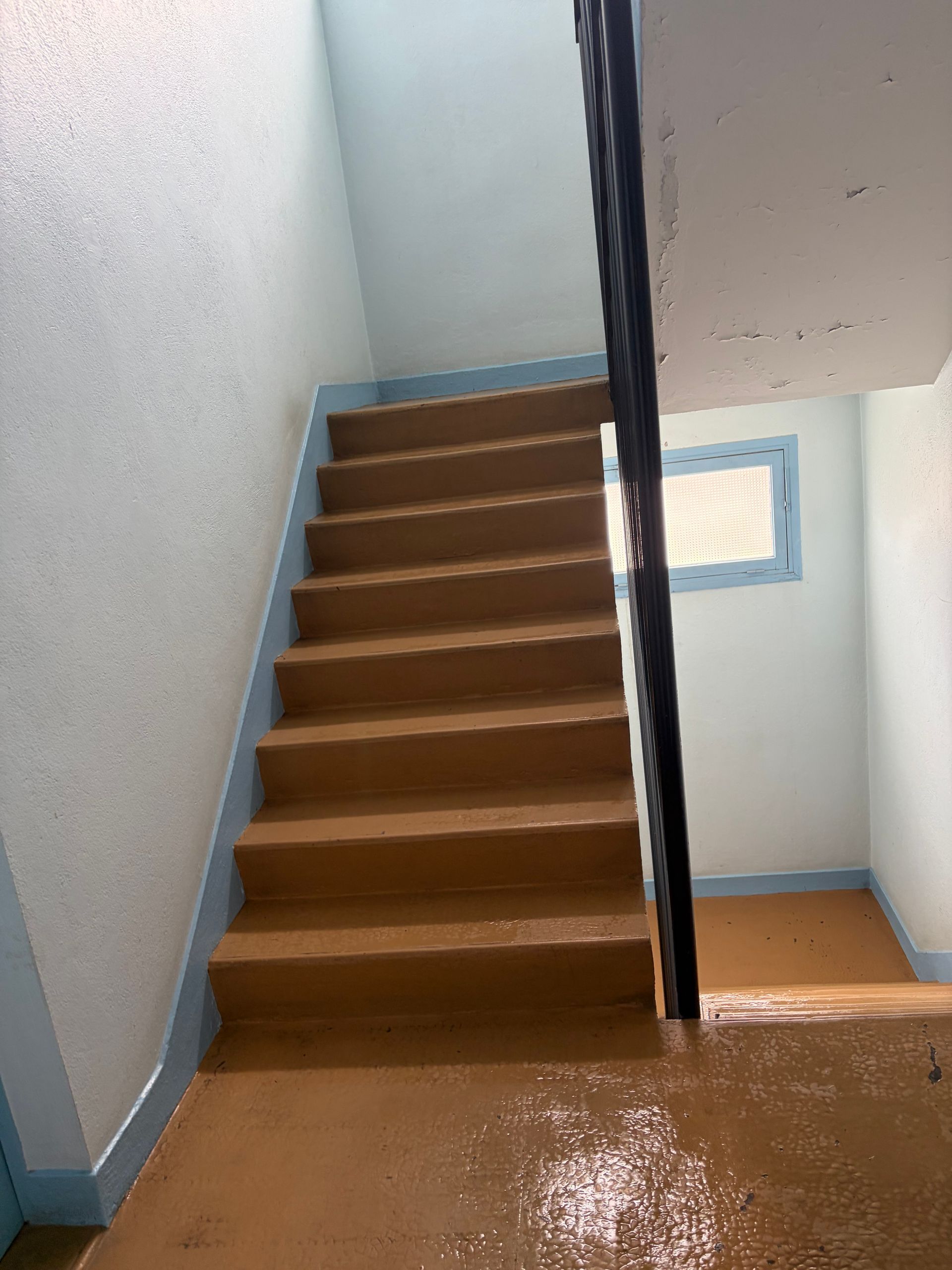 Une personne passe la serpillière sur le sol marron brillant d'un couloir, à côté d'un mur beige.