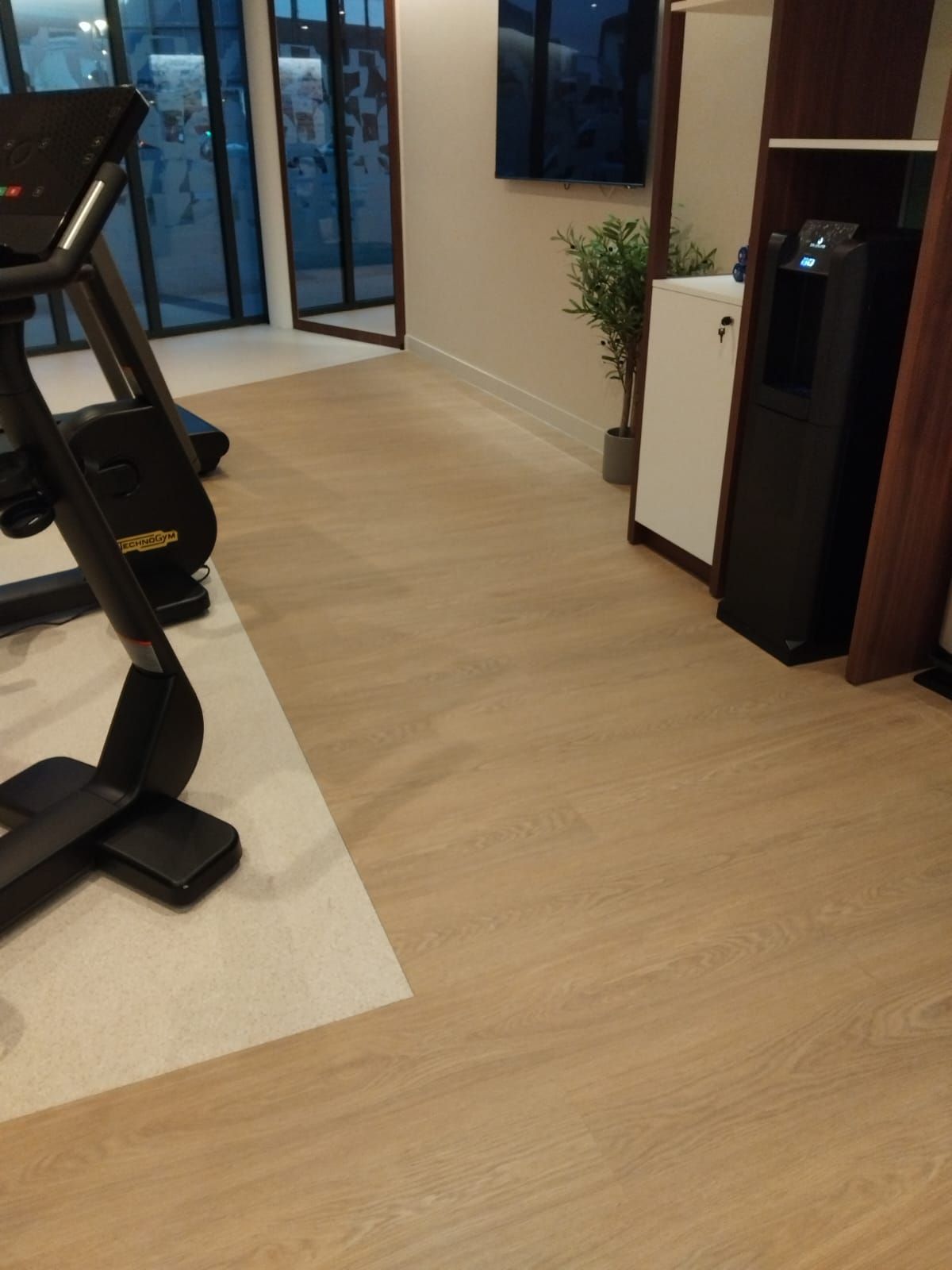 Salle de sport avec tapis roulant sur parquet et portes vitrées donnant sur l'extérieur.