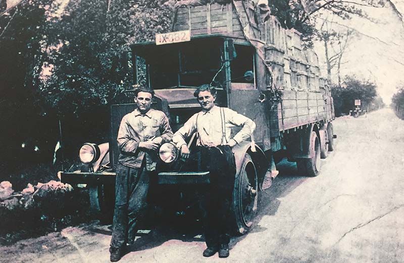 Ein Schwarzweißfoto von zwei Männern, die neben einem Lastwagen stehen