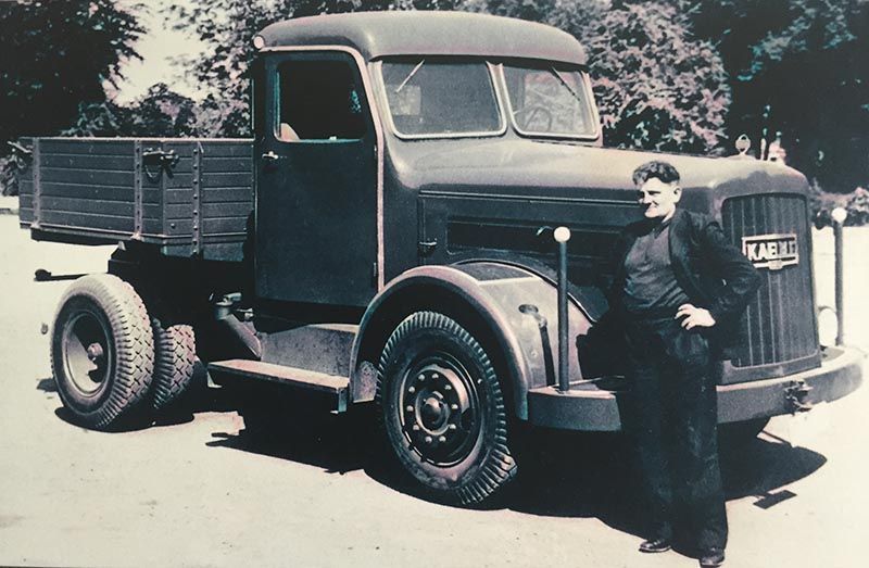 Ein Schwarzweißfoto eines Mannes, der neben einem LKW steht, auf dem Kamt steht