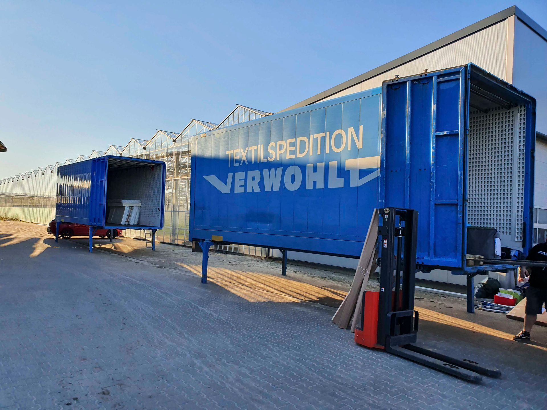 Zwei blaue Schiffscontainer stehen nebeneinander auf einem Parkplatz.