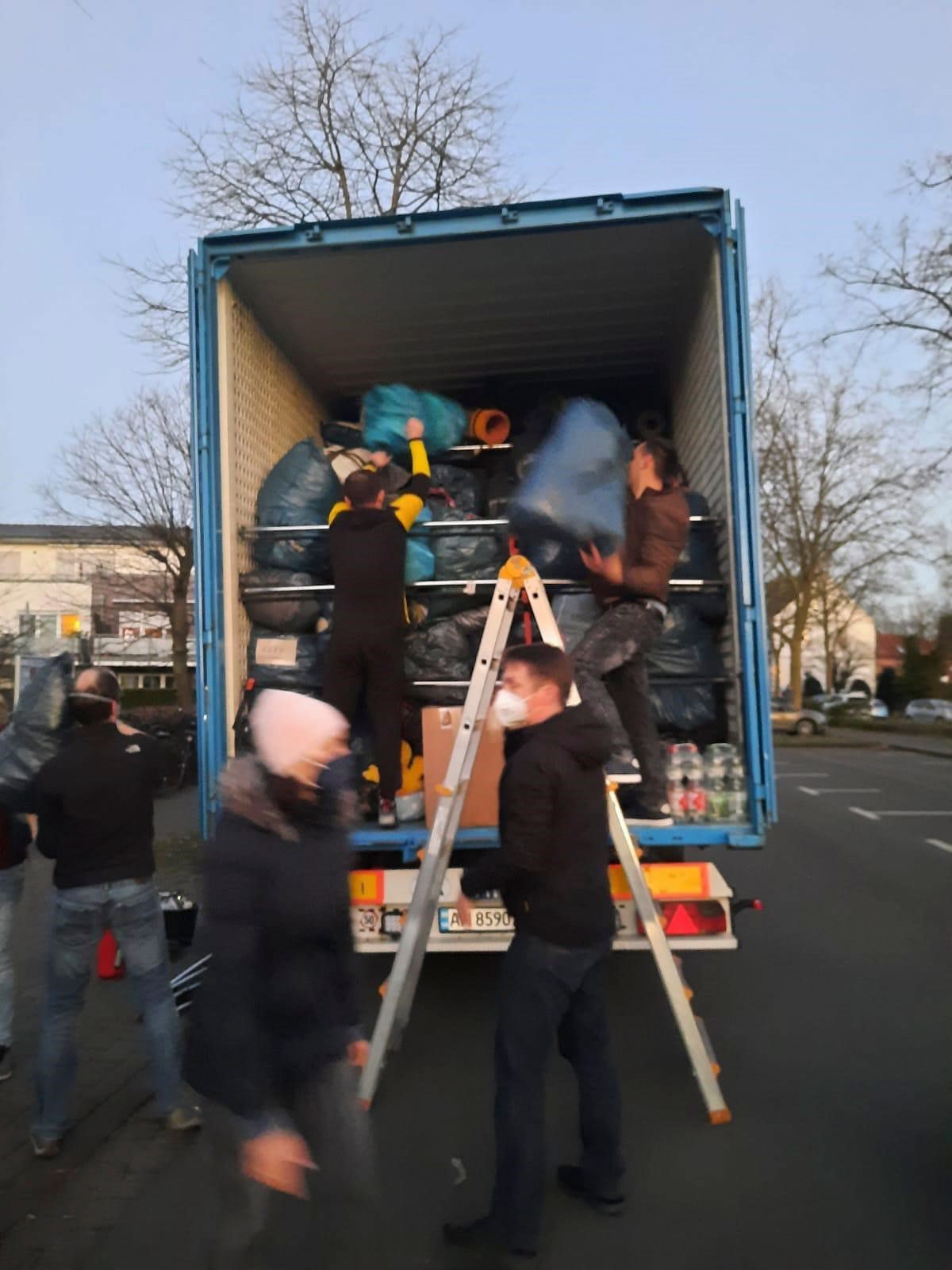 Eine Gruppe von Leuten belädt einen LKW mit einer Leiter.