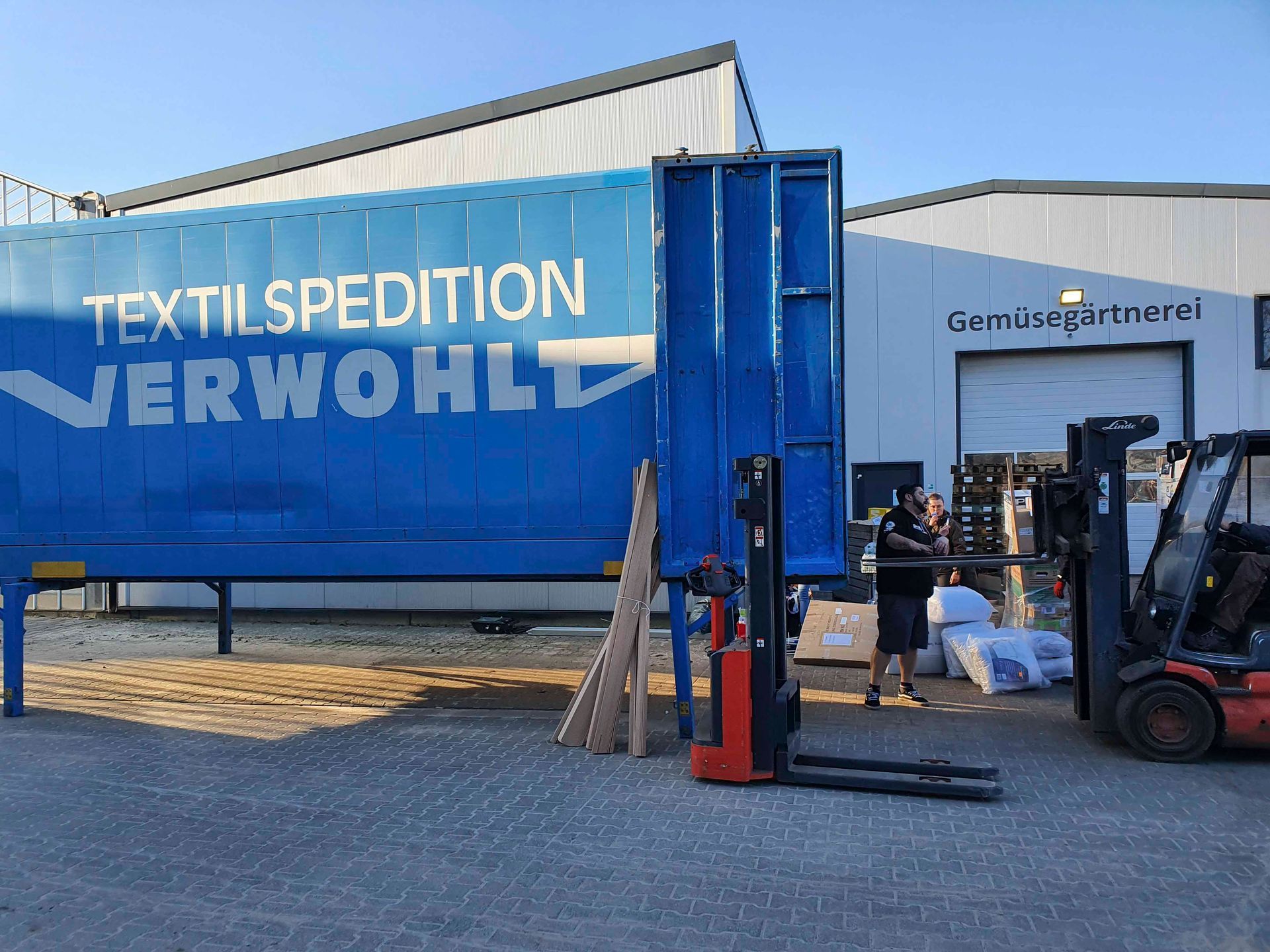 Ein Mann steht vor einem blauen LKW mit der Aufschrift „Textilspedition verwohl“