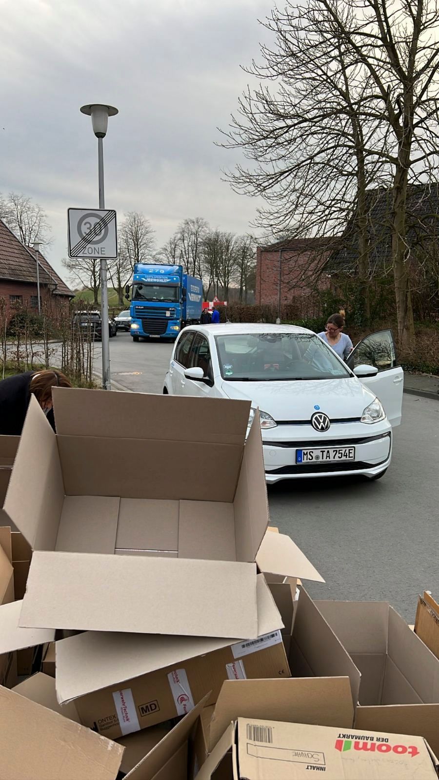 Ein weißes Auto fährt eine Straße entlang neben einem Stapel Pappkartons.
