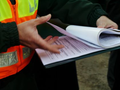 Eine Person in einer orangefarbenen Weste hält ein Klemmbrett und ein Blatt Papier.