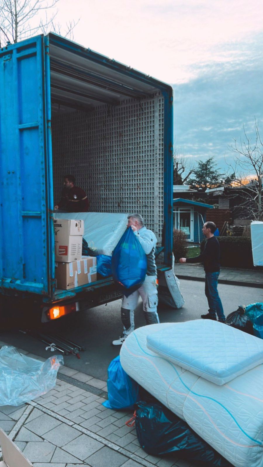 Ein Mann lädt eine Matratze in einen blauen Lastwagen.