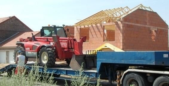 Un chariot élévateur rouge de chantier sur une remorque bleue, sur un chantier de construction de maison en briques.