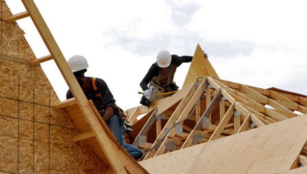 Des ouvriers du bâtiment, casqués, construisent un toit à l'extérieur, utilisant des scies et du contreplaqué.