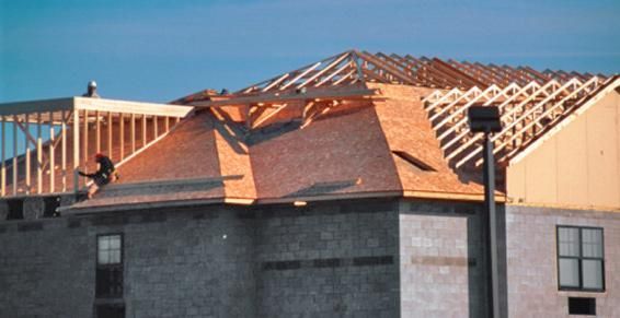 Des ouvriers du bâtiment travaillent sur un toit, posant des bardeaux et une charpente en bois. Bâtiment en construction.