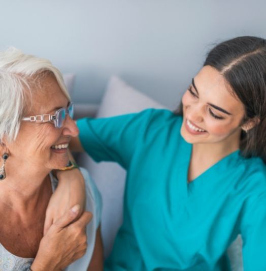 Eine Krankenschwester spricht mit einer älteren Frau auf einer Couch.