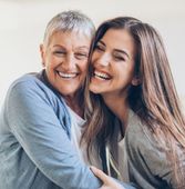 Eine ältere und eine jüngere Frau umarmen sich und lächeln.