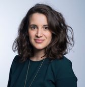 Eine Frau in einem grünen Hemd und einer Halskette lächelt in die Kamera
