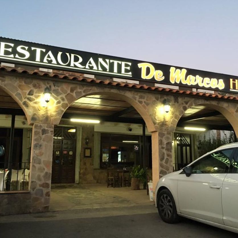 Un coche blanco está aparcado delante de un restaurante llamado Restaurante de Marcos.