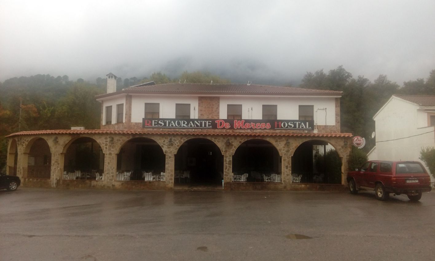 Un restaurante con coches aparcados delante en un día nublado.