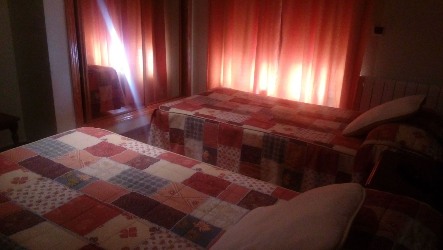 Un dormitorio con dos camas y una ventana con cortinas rojas.