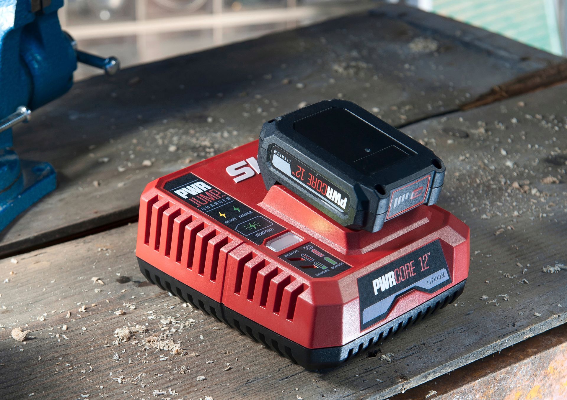 Un chargeur de batterie SKIL PWRCore 20 rouge avec une batterie noire fixée, posé sur un établi en bois.