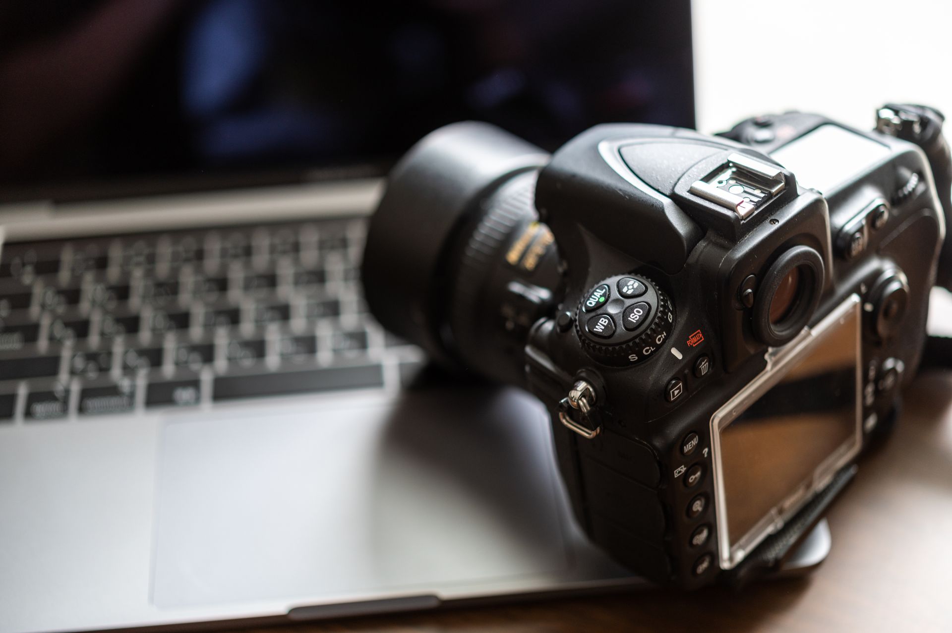 Appareil photo reflex numérique noir avec objectif, posé sur le clavier d'un ordinateur portable.