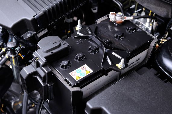 Batterie de voiture dans le compartiment moteur. Noire, rectangulaire, avec bornes visibles et étiquettes d'avertissement.