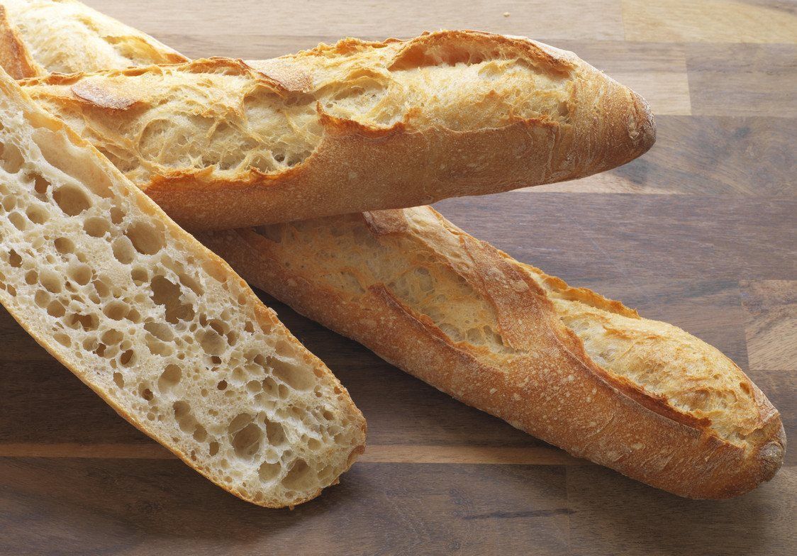 Deux baguettes croustillantes, l'une coupée en deux dans le sens de la longueur pour révéler une mie aérée, reposent sur une surface en bois.