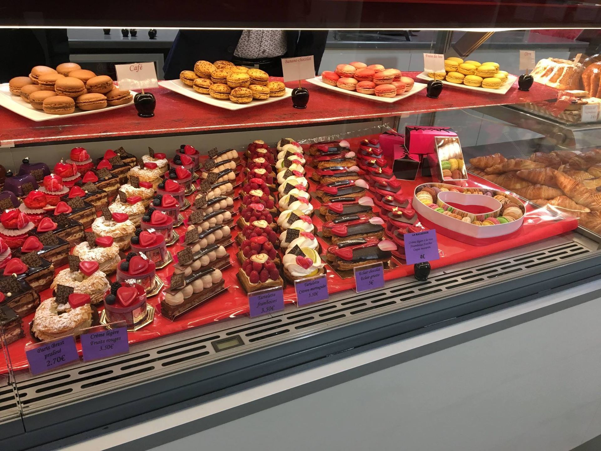 Une vitrine remplie de rangées de pâtisseries françaises assorties, de macarons colorés et de desserts en forme de cœur.