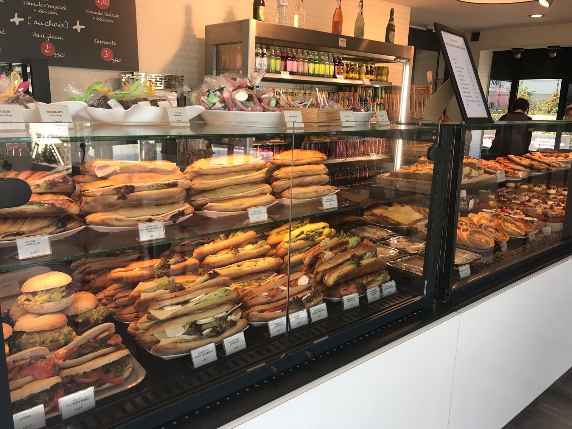 Une vitrine dans une boulangerie, remplie de sandwichs et de pâtisseries variés disposés sur plusieurs étagères.
