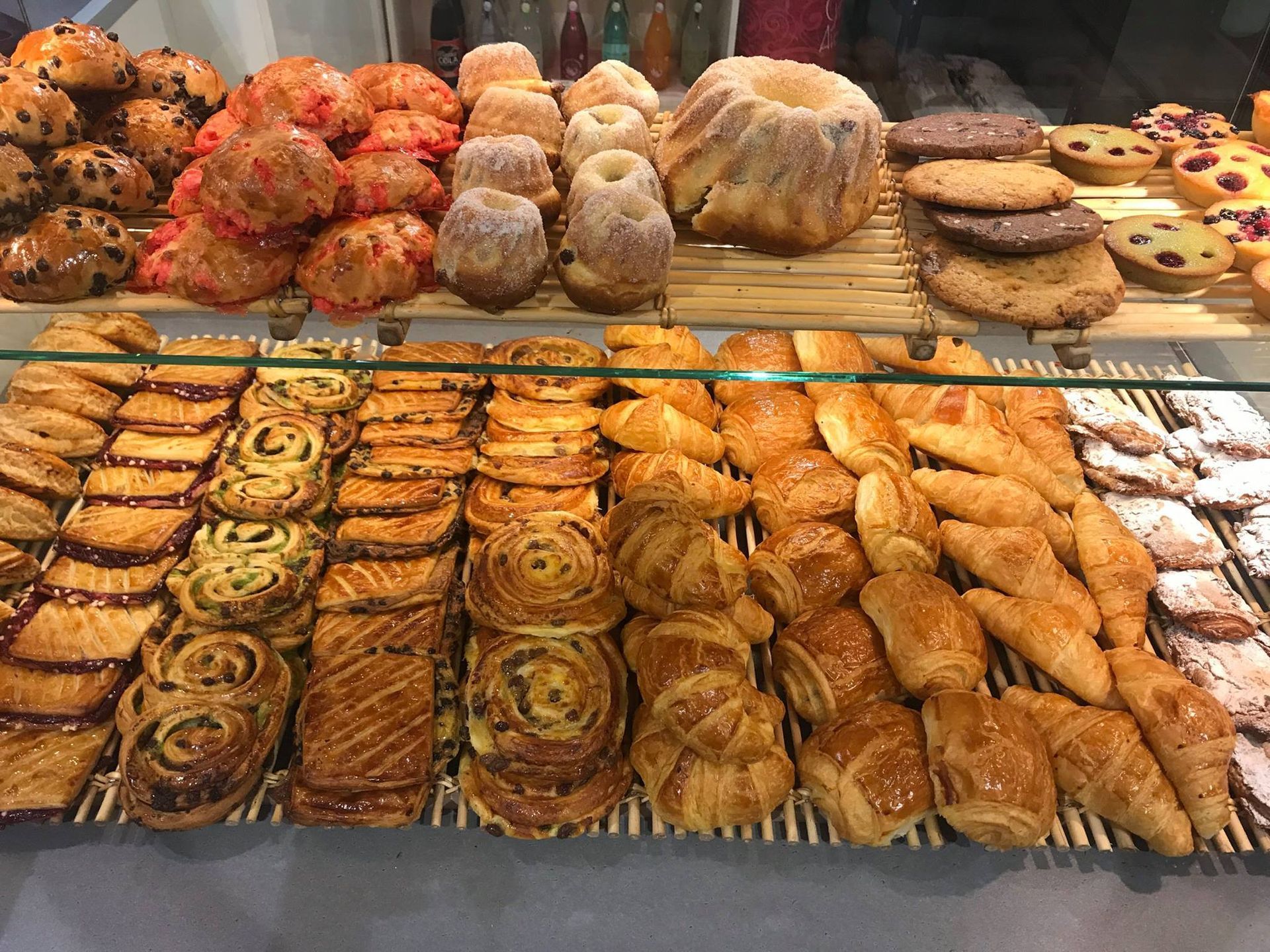 Une vitrine remplie de rangées de viennoiseries dorées assorties, notamment des petits pains, des biscuits et des croissants.