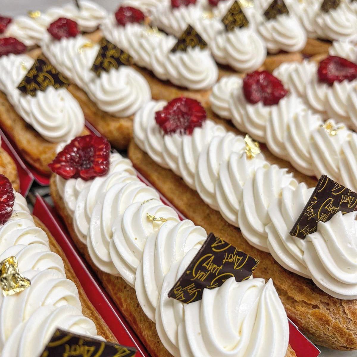 Des rangées d'éclairs fourrés à la crème, garnis de glaçage blanc, de framboises fraîches et de décorations en chocolat.