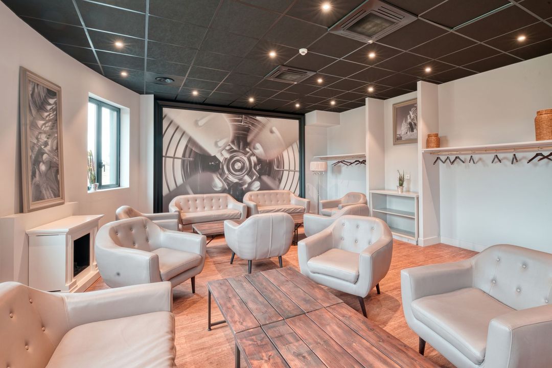 Un coin salon moderne avec des fauteuils gris, une table basse en bois et un plafond noir avec éclairage encastré.